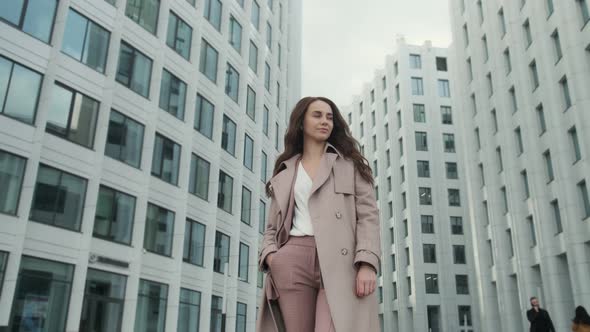 Smiling girl with brown hair stands at the corporate building for a break, dressed in an elegant