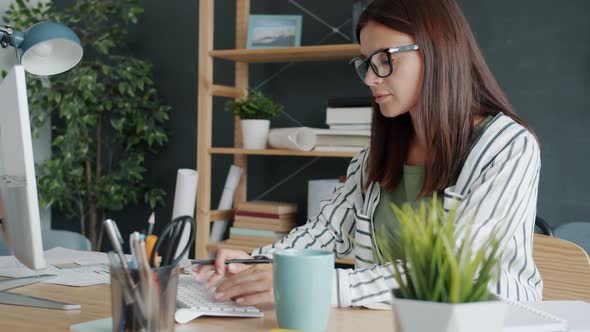 Portrait of Busy Young Architect Looking at Construction Plans on Paper and Using Computer in Office