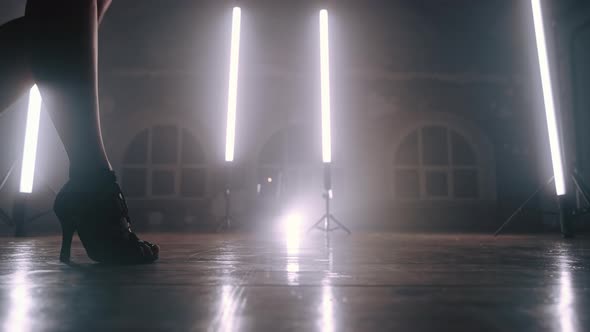 Woman in Heels Walks Near Camera Across Long Lamps in Smoky Studio