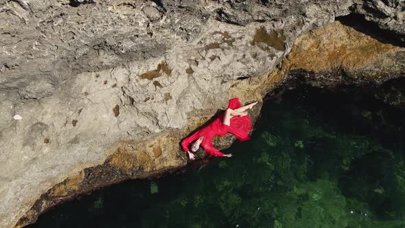 Woman in a Red Long Dress Lies on a Rock