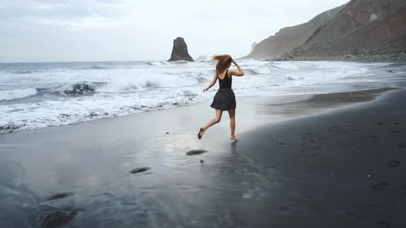 Young Woman in a Beautiful Dress Runs Along the Black Volcanic Black Sand Beach Benijo in the North