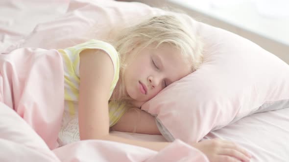 Adorable Blonde Girl Sleeping Sweetly in the Morning on Pink Bed Linens at Home