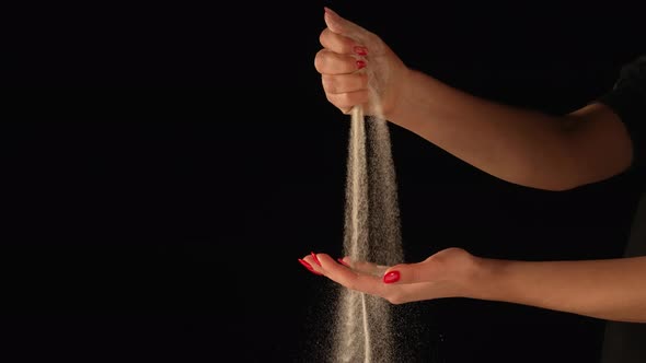 Stream of Dry Sand Pours Into Palm of Woman and is Spilling Through Her Fingers on Black Background