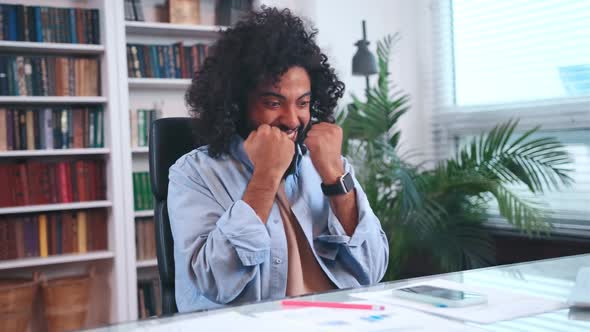 Overjoyed Arabian Man Student Rejoices Sits in Front of Desk in Home Office