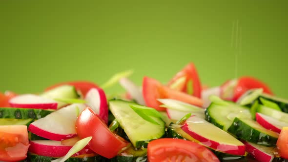 Pouring olive oil on fresh vegetables salad, green background