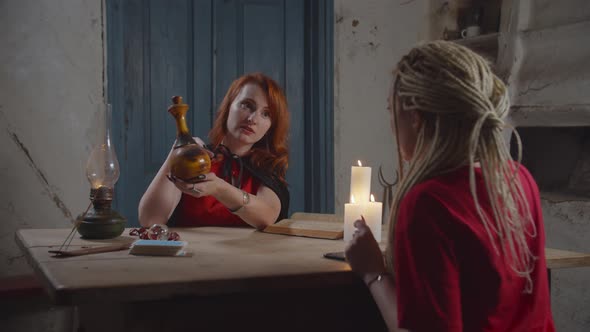 White Witch Giving Love Potion To Woman Indoors