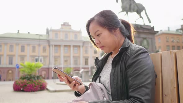 Asian woman sitting and using smartphone in town with big building background