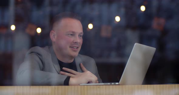 A Man Is Sitting In A Cafe And Talking On Video Via Laptop