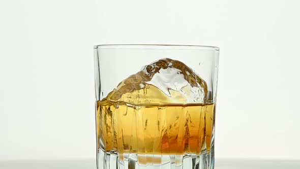 One big ice rock spins in whiskey glass on white