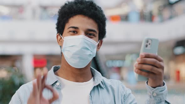 Portrait African Dominican Guy Sick Man in Protective Medical Mask with Phone Showing Ok Gesture at