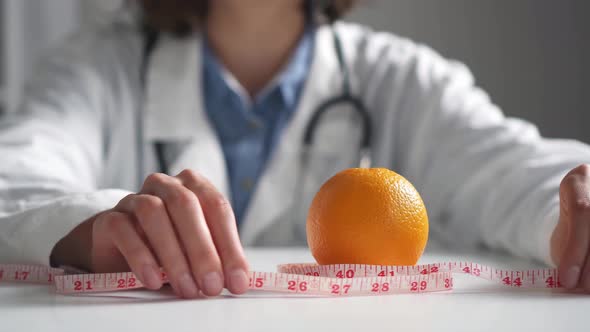 Doctor Nutritionist Measuring Tape Tightens Orange Fruit. Close Up Of A Diet Doctor Pulling