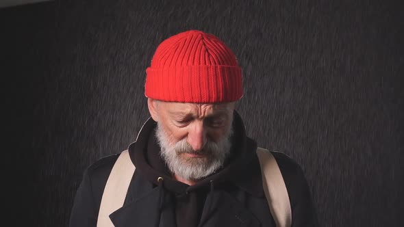 Homeless Mature Bearded Man Stands in the Rain Holding a Cup To Collect Money.