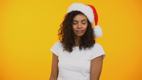 Cute Curly-Haired Girl in Santa Hat Showing Hush, Holding Red New Years Giftbox