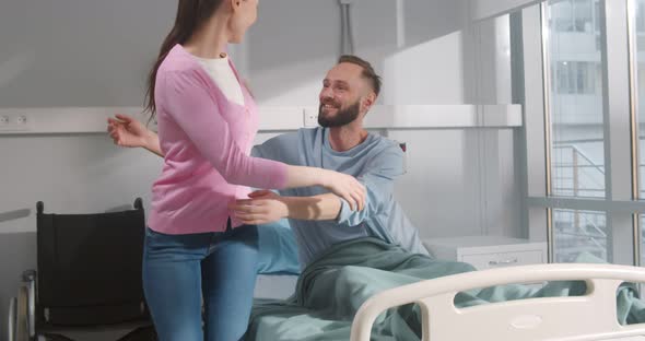 Young Wife Visiting and Hugging Sick Husband Lying in Hospital Bed