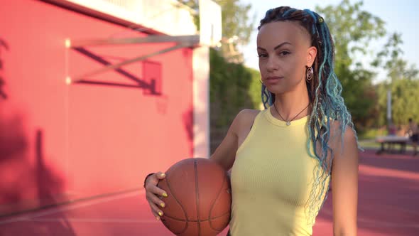 A Young Woman Holds a Basketball on the Background of a Basketball Court