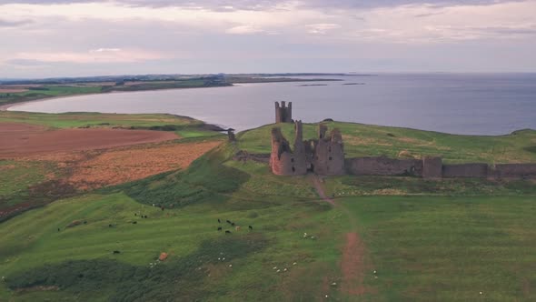 Dunstanburgh Castle at sunset, a famous landmark in Northumberland, England, UK. Aerial drone view