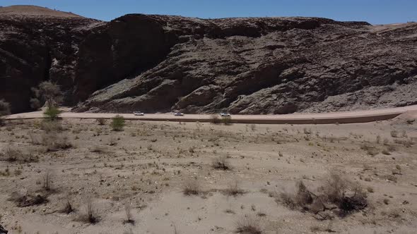 Massive rocky mountain and desert plants with three cars driving on a road