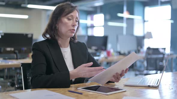 Serious Middle Aged Businesswoman Reading Paper and Talking While Sitting in Office