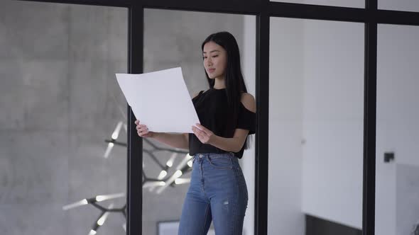 Portrait of Smiling Confident Slim Asian Businesswoman Analyzing Paperwork Standing in Office