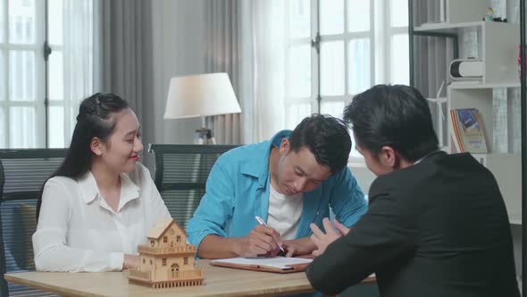 Asian Man With A Woman And Real Estate Agent Signing On House Purchase Contract Paper