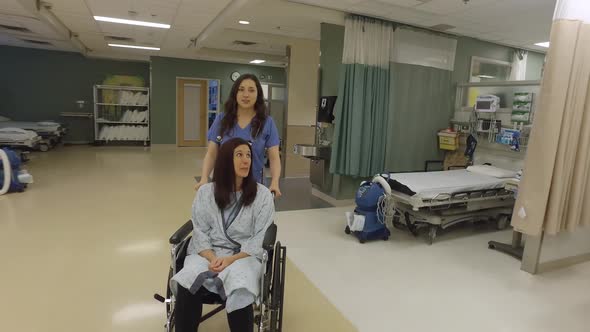 Friendly nurse talks to and pushes a female patient in a wheelchair.