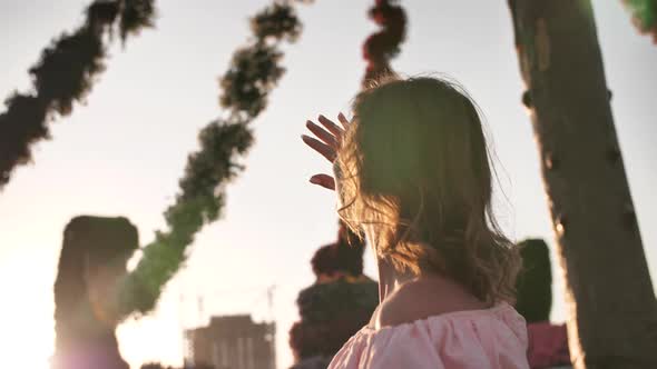 Girl Admires Hanging Flowers in a City Park