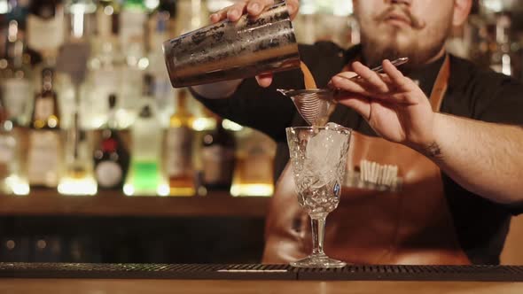 Bartender Is Filtering Mixed Drink Into Glass for Serving Closeup of His Hands