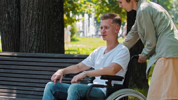 Friends Walking in Park a Guy in a Wheelchair Talking with His Girlfriend and He Sits Next to Him on