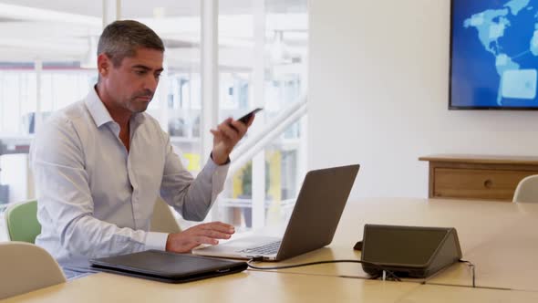 Businessman talking on mobile phone while using laptop in a modern off 4k