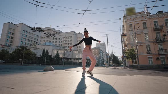 Young Woman Enjoys Dancing on City Square at Back Sunrise