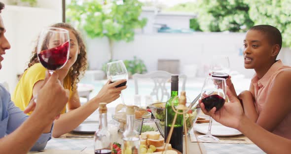 Group of diverse male and female friends laughing and drinking wine together at dinner party