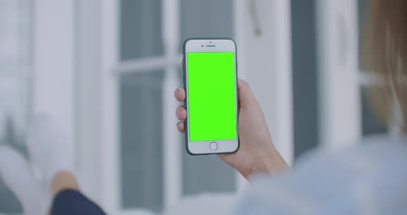 Over Shoulder Shot of Woman Holding a Mobile Phone or Smartphone with a Vertical Green Screen in Her