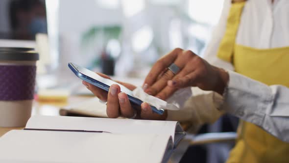 Woman wearing face mask wiping her smartphone with a tissue