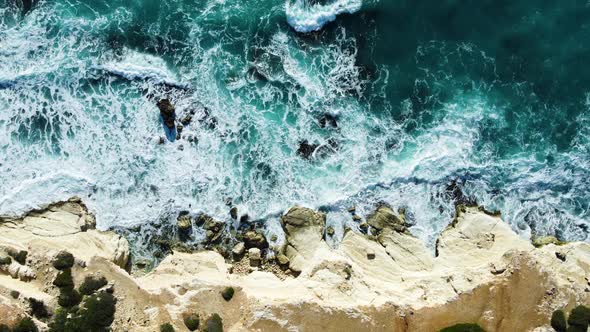 Sea Washes the Rocky Shore Above Aerial Shot Flying Over Coastline Cliffside with Blue Pure Water