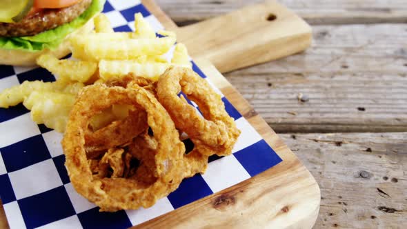 Hamburger, onion ring and french fries on chopping board