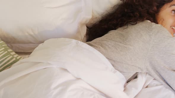 Happy young woman lying on bed using her mobile phone