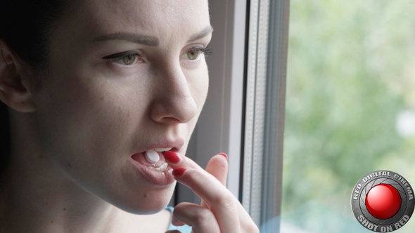 Face Of Woman Taking A Tablet And Drinking A Glass Of Water Standing By The Window