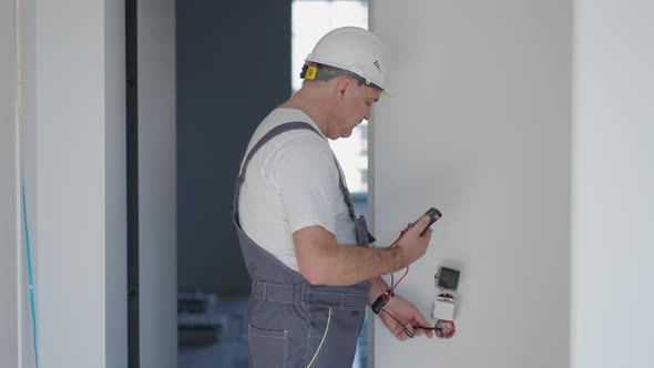 A Man Electrician in a Helmet in the Apartment Checks the Work of Sockets and Switches After Repair