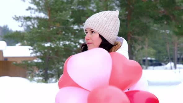 Happy woman throws up heart-shaped balloons outdoor in winter with snow. Valentine's Day