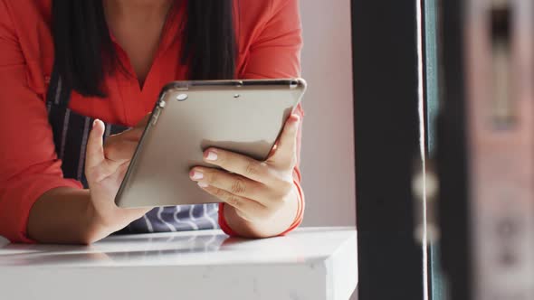 Video of midsection of biracial waitress using tablet at coffee shop