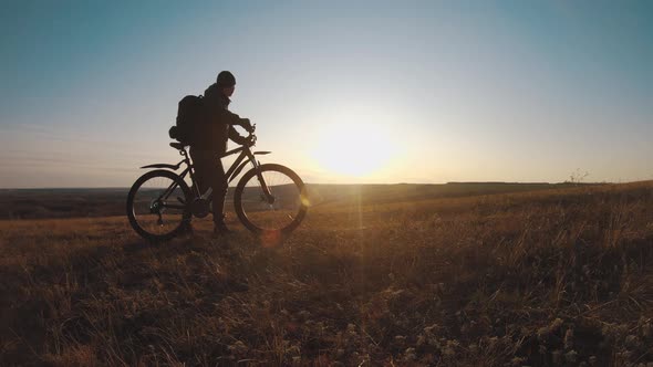 The Silhouette of the Mountain Bicycle Rider on the Hill with Bike at Sunset, Sport, Travel and