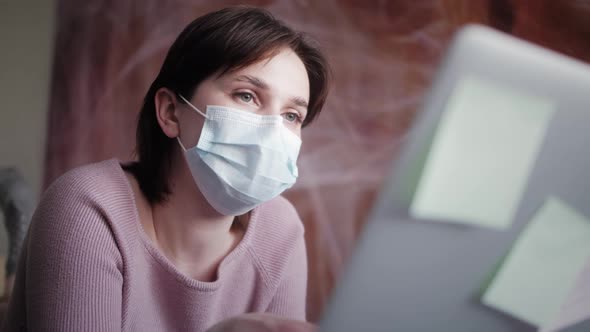 Young Woman in Medical Mask Studying or Working at Home Using Laptop Typing Message Writing Post