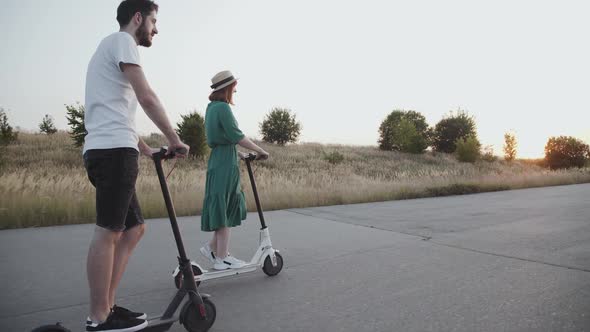 Girl in Dress and Boy Riding on Electric Scooters and Having a Fun on the Way