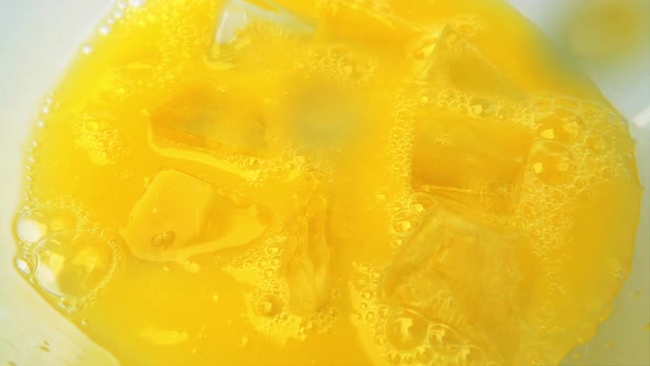 Pouring orange juice into a glass with ice. Slow motion.