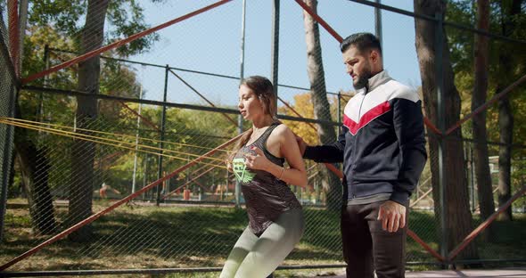 Sporty Woman with Personal Trainer Doing Exercises with Resistance Band Outside