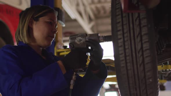 Female mechanic changing tires of the car using a power drill at a car service station