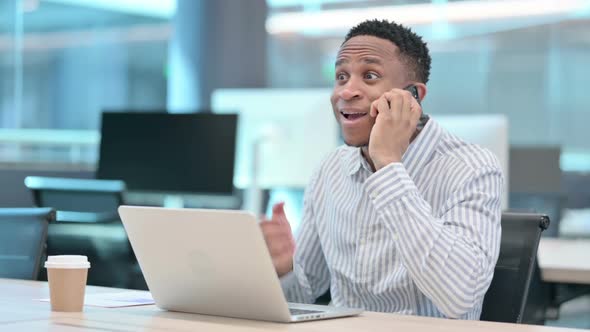 Angry African Businessman with Laptop Talking on Smartphone