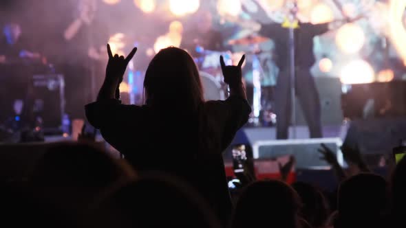 Silhouette of Woman in Crowd at Rock Concert Showing Sign Devil's Horns Gesture