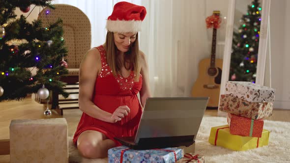 Happy Pregnant Woman Using Laptop on Christmas Eve at Home