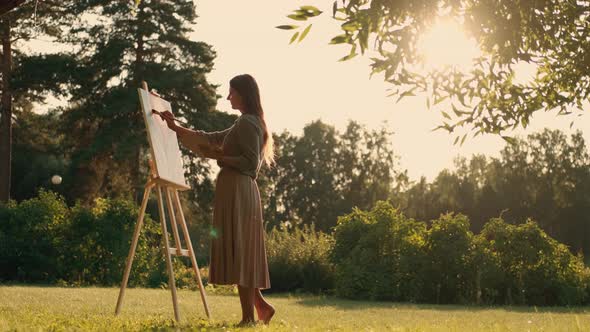 Creative Woman Artist Paints a Picture with a Brush While Standing Near the Easel in Nature